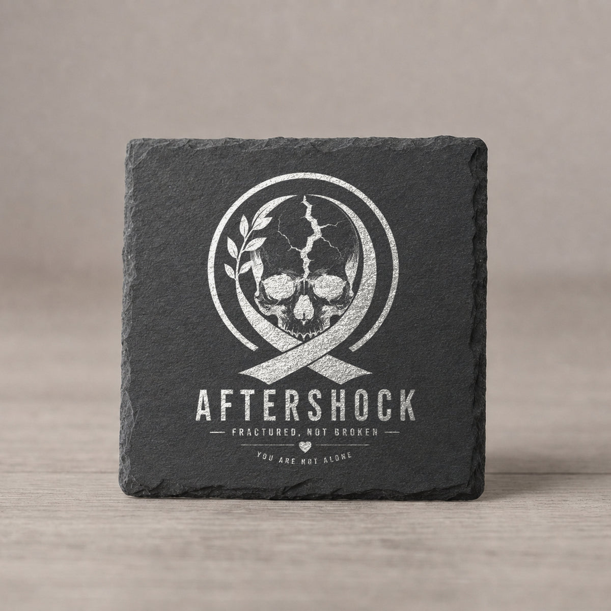 Black slate coaster laser engraved with the one-color Aftershock logo